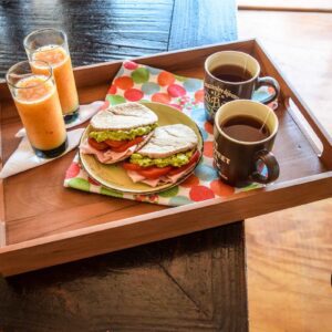 Bandeja de desayuno puma, fabricada en roble reciclado, presentada con un desayuno con jugo, tazas de te y pan pita relleno, fabricada en