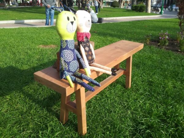 Banca Loica sobre pasto con 2 muñecos de tela sentados, fabricada en roble reciclado