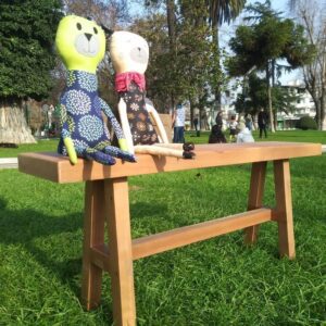 Banca Loica sobre pasto con 2 muñecos de tela sentados, fabricada en roble reciclado