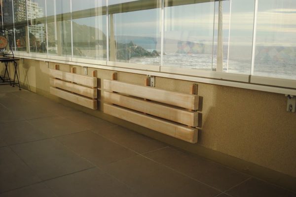 Bancas de pared fabricadas en mañio, con sistema plegable y con acabado en albayalde. Vista de las bancas plegadas en la terraza del cliente