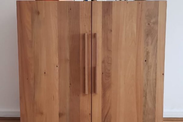 Mueble Bar Zorro cerrado, fabricado en madera de roble reciclado. Fotografía en uso en la casa del cliente. Cuenta con dos puertas, cerradas en la imagen, ambas con espacio para botellas, cuelga copas en su interior y espacio para 8 botellas de vino acostadas en la parte inferior.
